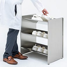 Person in lab coat using cleanroom shoe rack to retrieve white shoes