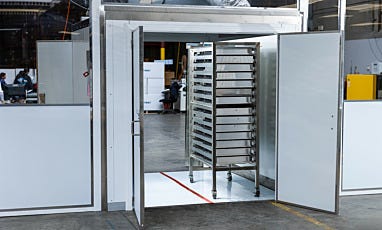 Humidity-controlled drying room with open doors and a rack of filters on a cart inside.