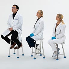 Three laboratory workers in white coats sitting on stainless steel lab stools in tall, medium, and short heights