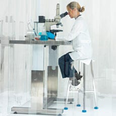 Scientist in white lab coat examining samples under microscope in enclosed cleanroom workstation