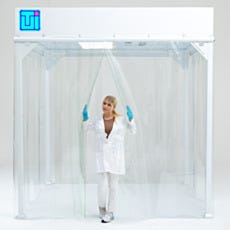 Laboratory Technician in White Coat Standing at Softwall Cleanroom Entry with Vinyl Strip Curtains