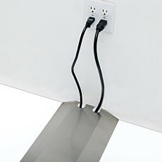 Photo of two cables emerging from slots in a steel floor raceway cover plugging into a wall outlet