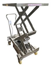 Stainless steel portable scissor lift table raised showing hydraulic system and safety warning label