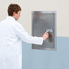 Laboratory technician operating combination lock on wall-mounted stainless steel storage cabinet
