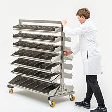 photo of a man in a lab coat moving a wheeled steel rack of shelves and storage bins