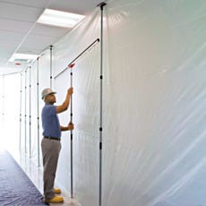 Construction worker in hard hat installing ZipWall dust barrier poles with plastic sheeting hallway