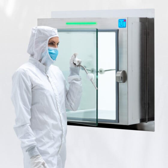 Cleanroom technician in protective gown opening full glass door of center wall mounted pass-through