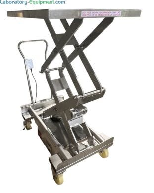 Stainless steel portable scissor lift table in raised position showing hydraulic mechanism, push handle, casters, and safety warning label on platform edg  |  1735-08 displayed